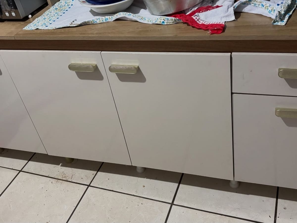 Balcão de cozinha branco com três portas e uma coluna de duas gavetas, tampo de madeira e pés plásticos, sobre piso de cerâmica branca.