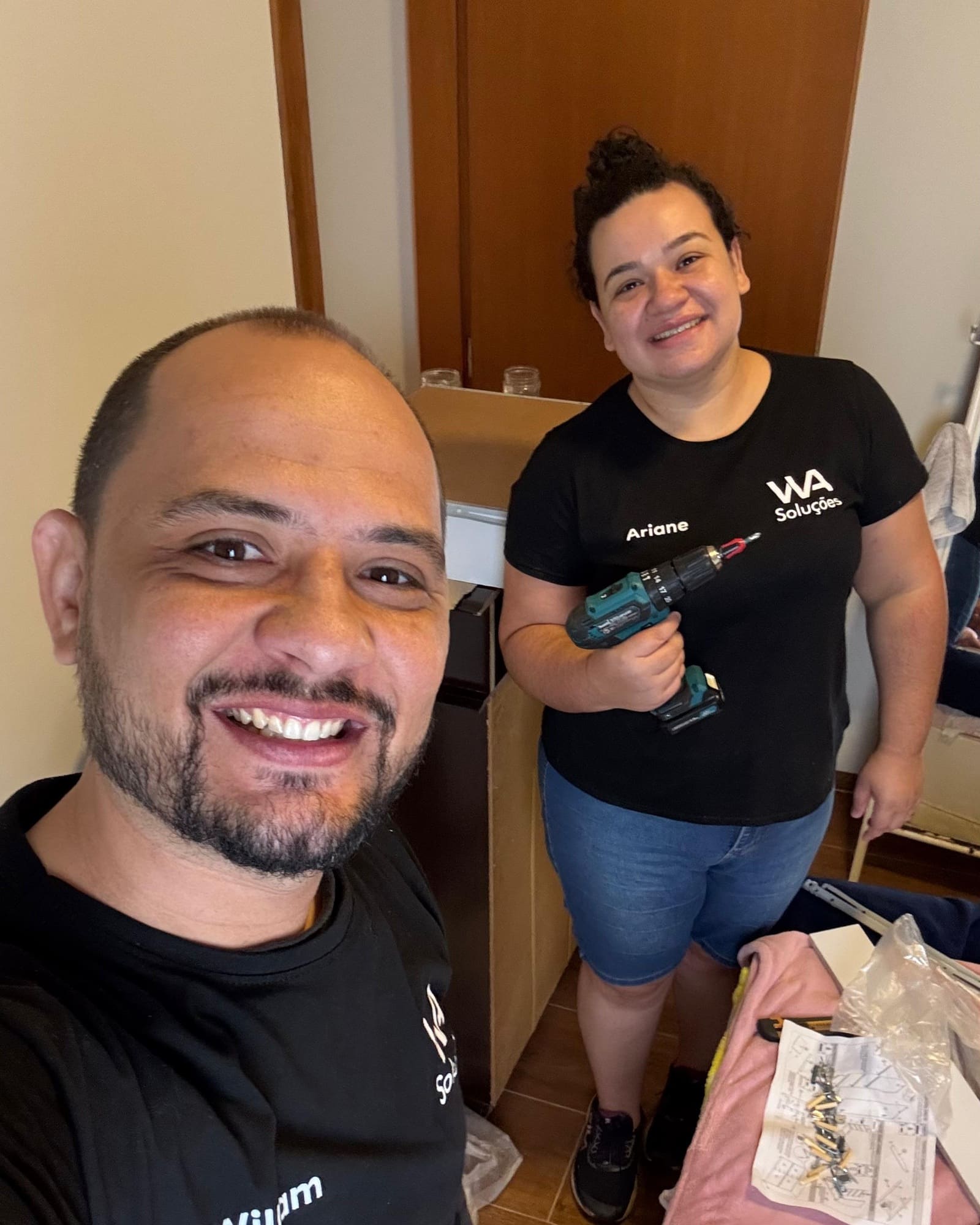 William e Ariane de camiseta da WA Soluções, com o nome bordado no peito, no meio de uma montagem; ela segura uma parafusadeira