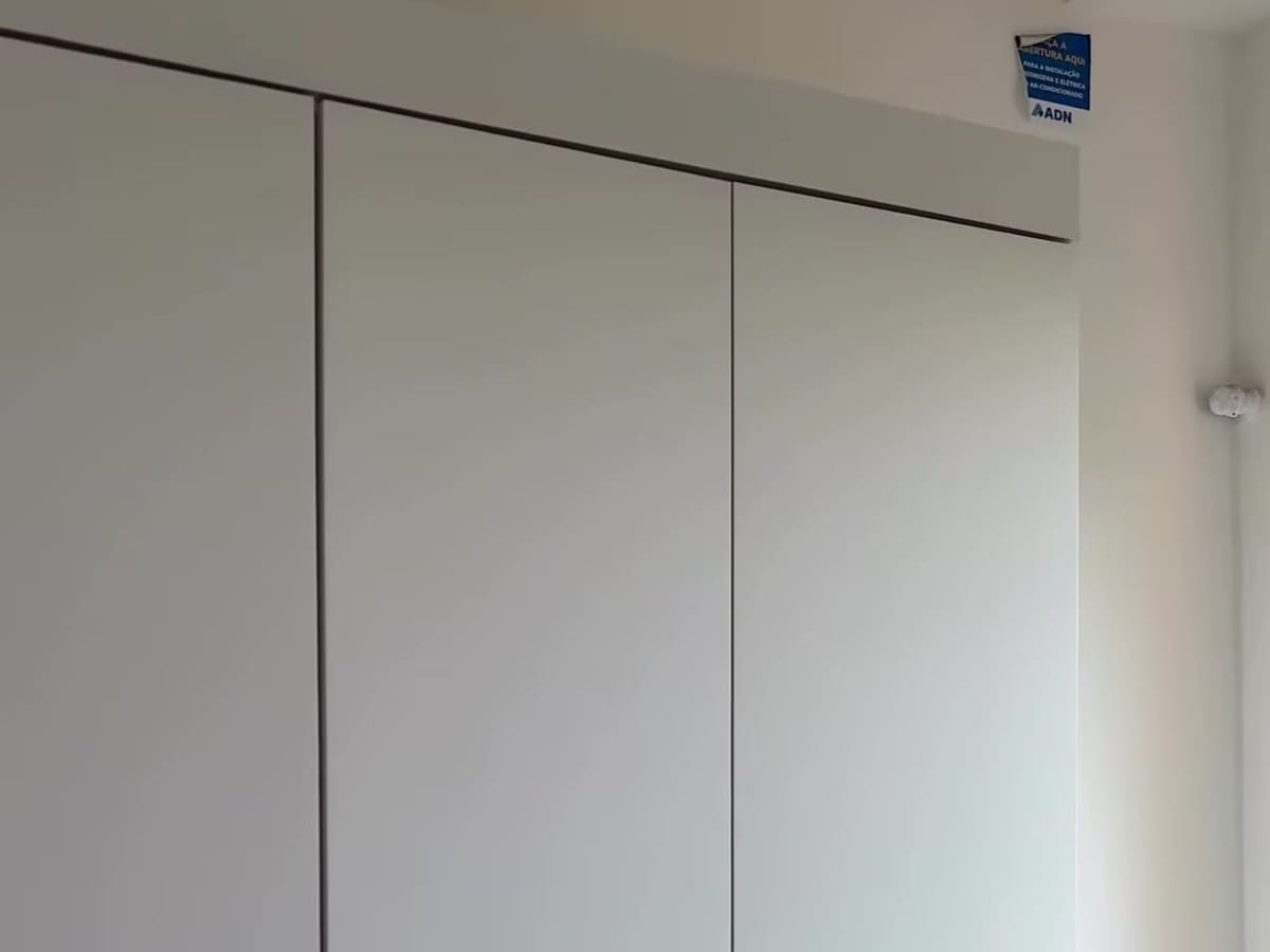 Guarda-roupa branco embutido que vai do chão ao teto, com portas lisas e as frestas entre elas alinhadas, no canto de um quarto recém-entregue.